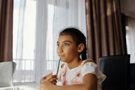 Thoughtful young girl sitting at desk indoors, pondering while holding a pencil.